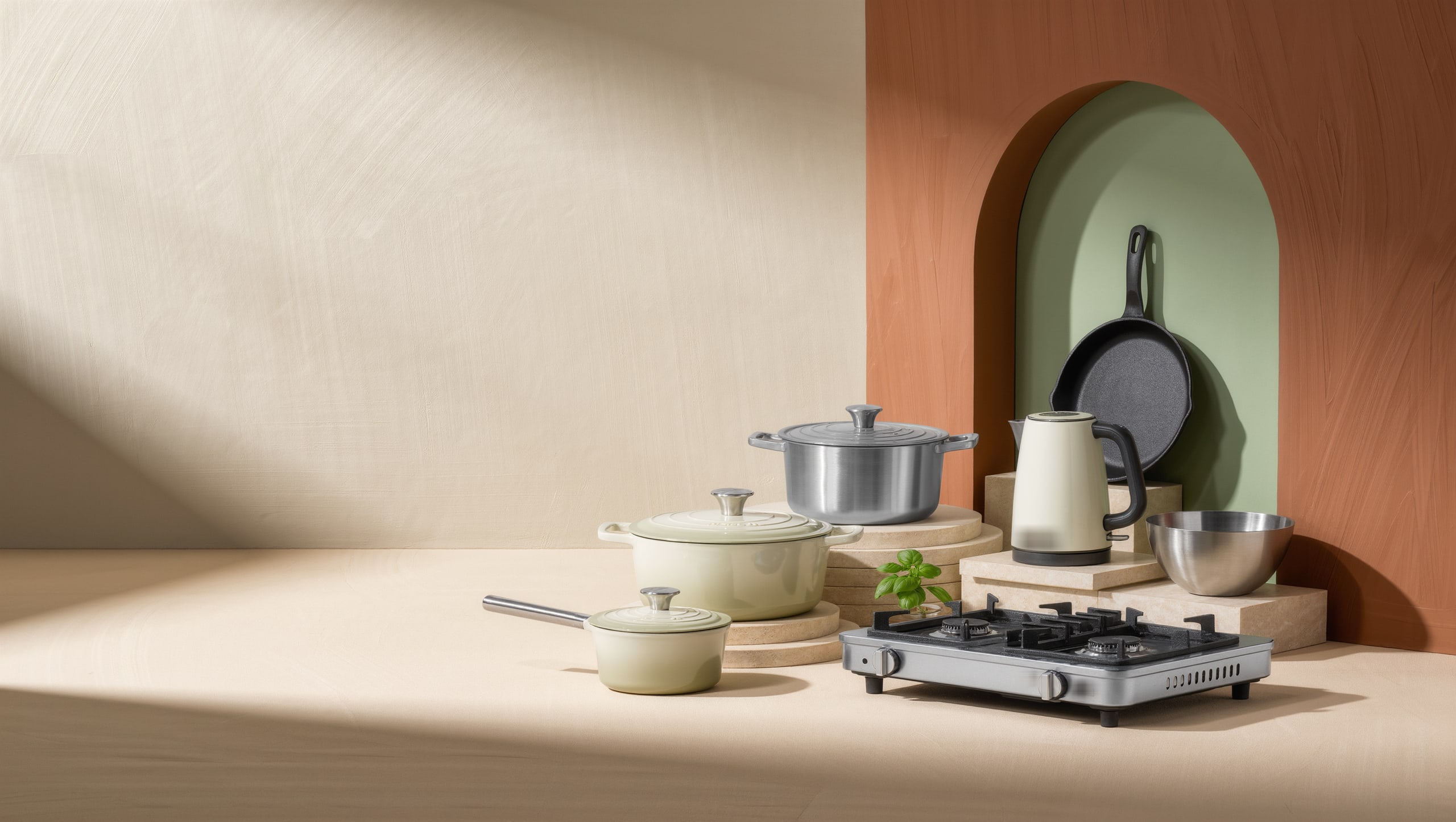 Cream enamelled cookware, a stainless steel stockpot, an electric kettle, a cast-iron frying pan and a two-burner gas stove staged on stone pedestals — kitchen essentials at Diplaxmi Kitchen Store.